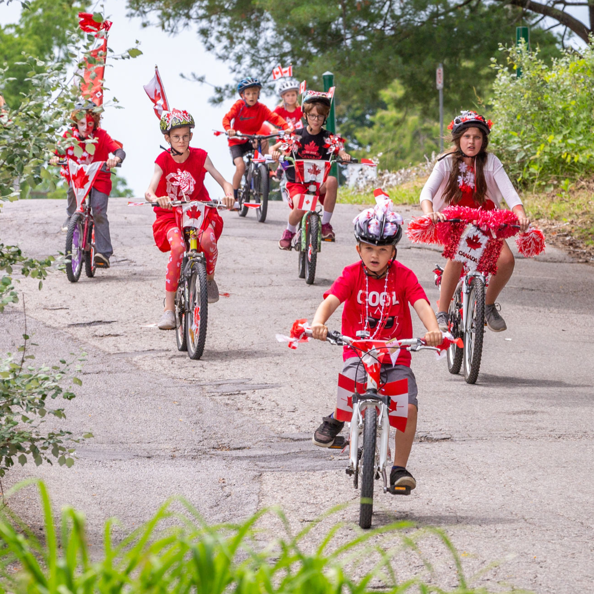 Kids riding bikes that are decorated in Canada red going down a hill