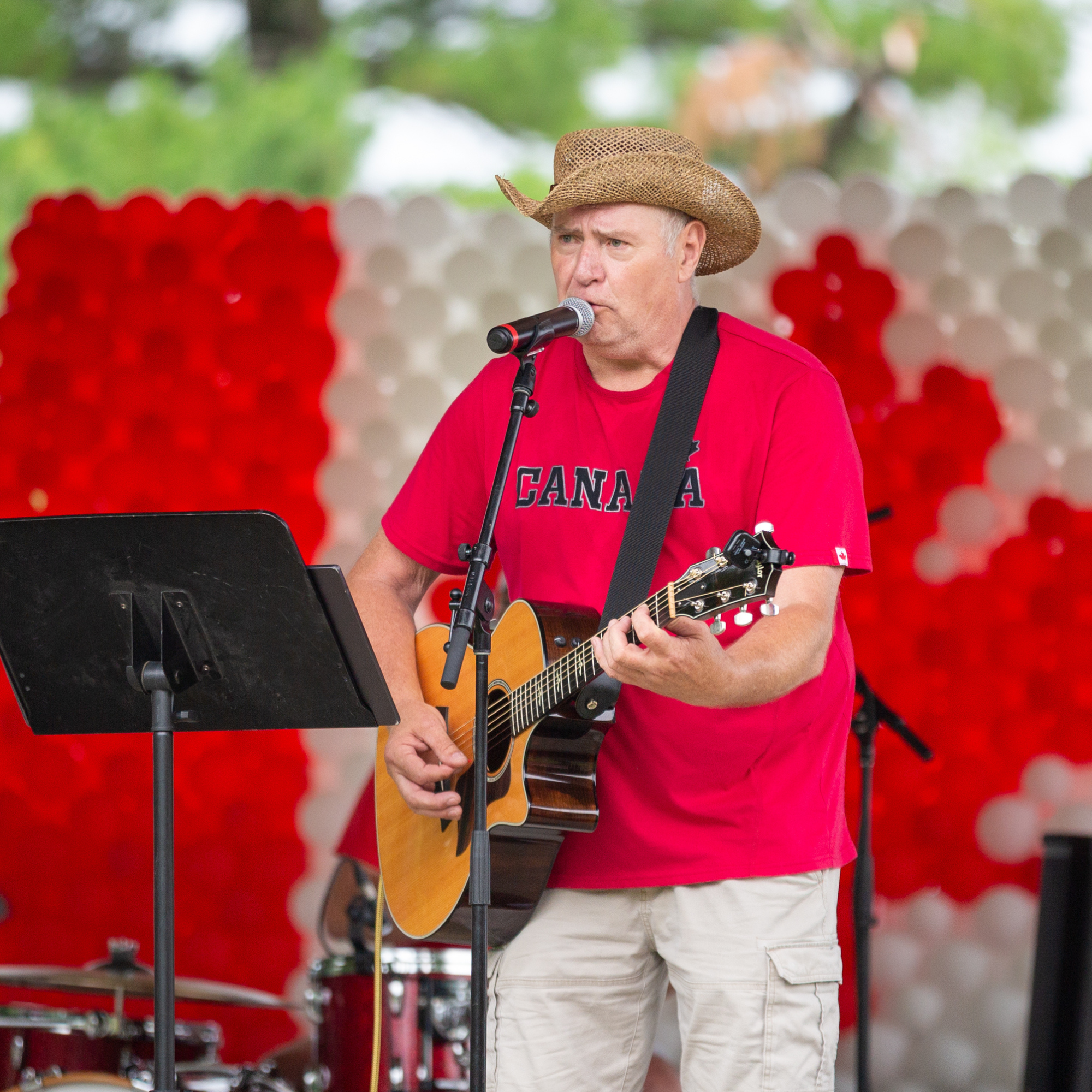 A man playing guitar and singing in a Canadian red shirt