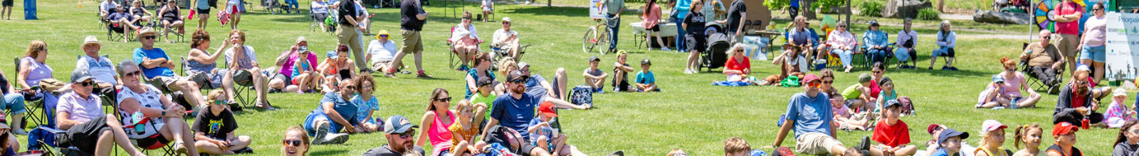 A crowd of people sit on the grass at Robert Simpson Park watching a performance