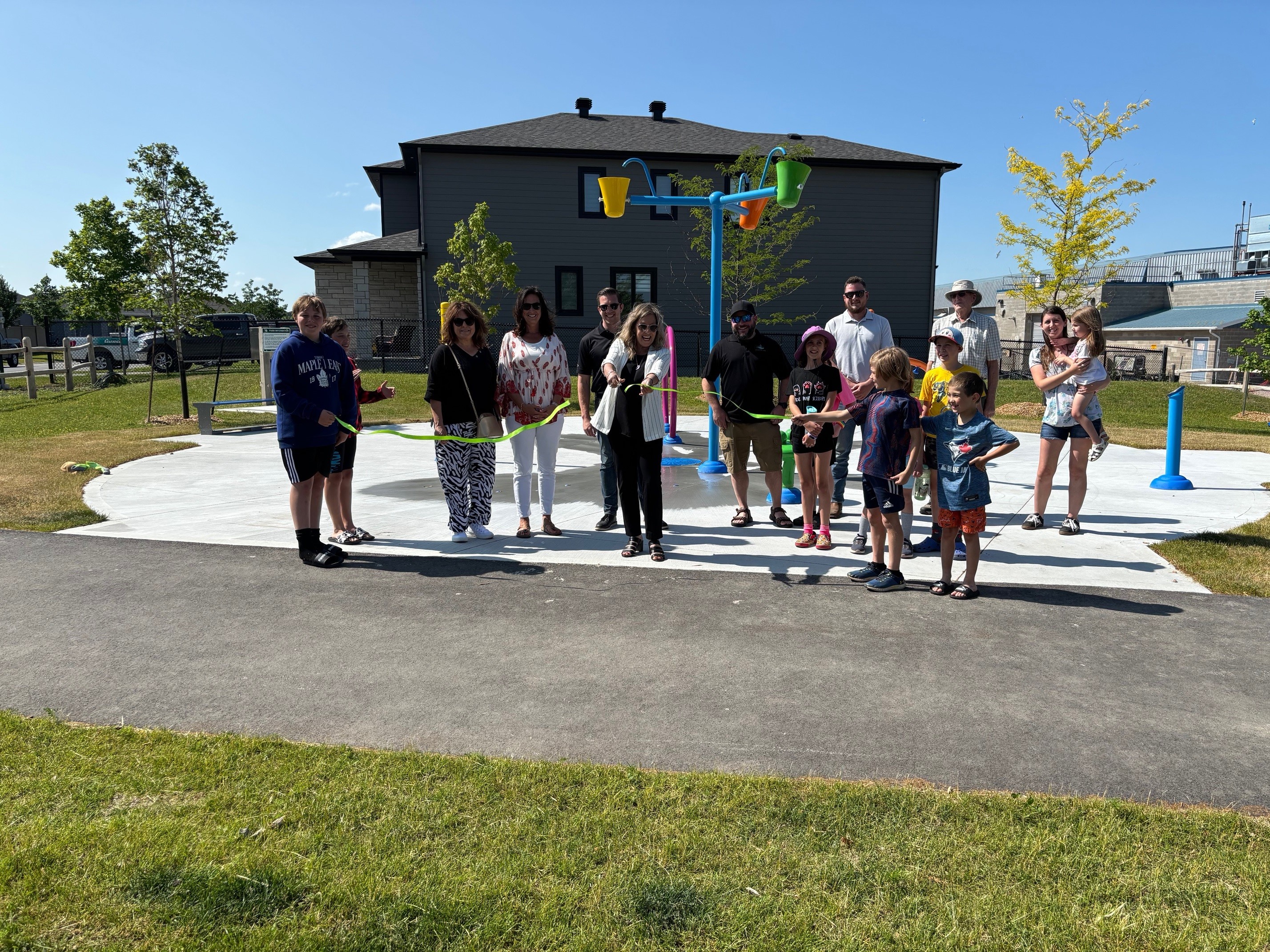 People standing in front of splash pad cutting ribbon