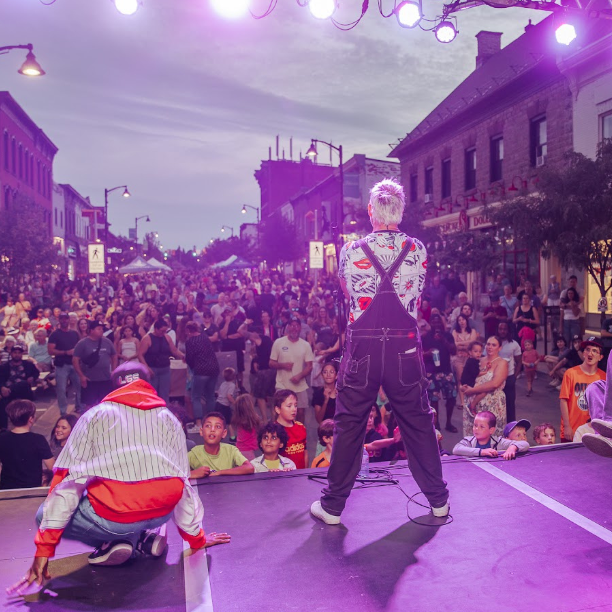 Three men on stage performing in front of a packed street of people
