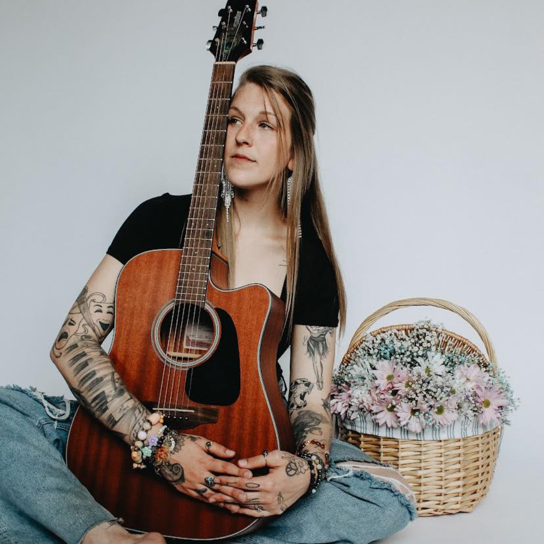 Vicki posing for a photo with her guitar while sitting on the floor