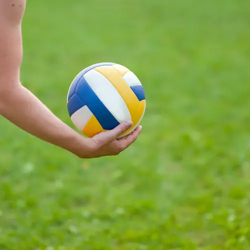 A person holding a volleyball in hand over grass 
